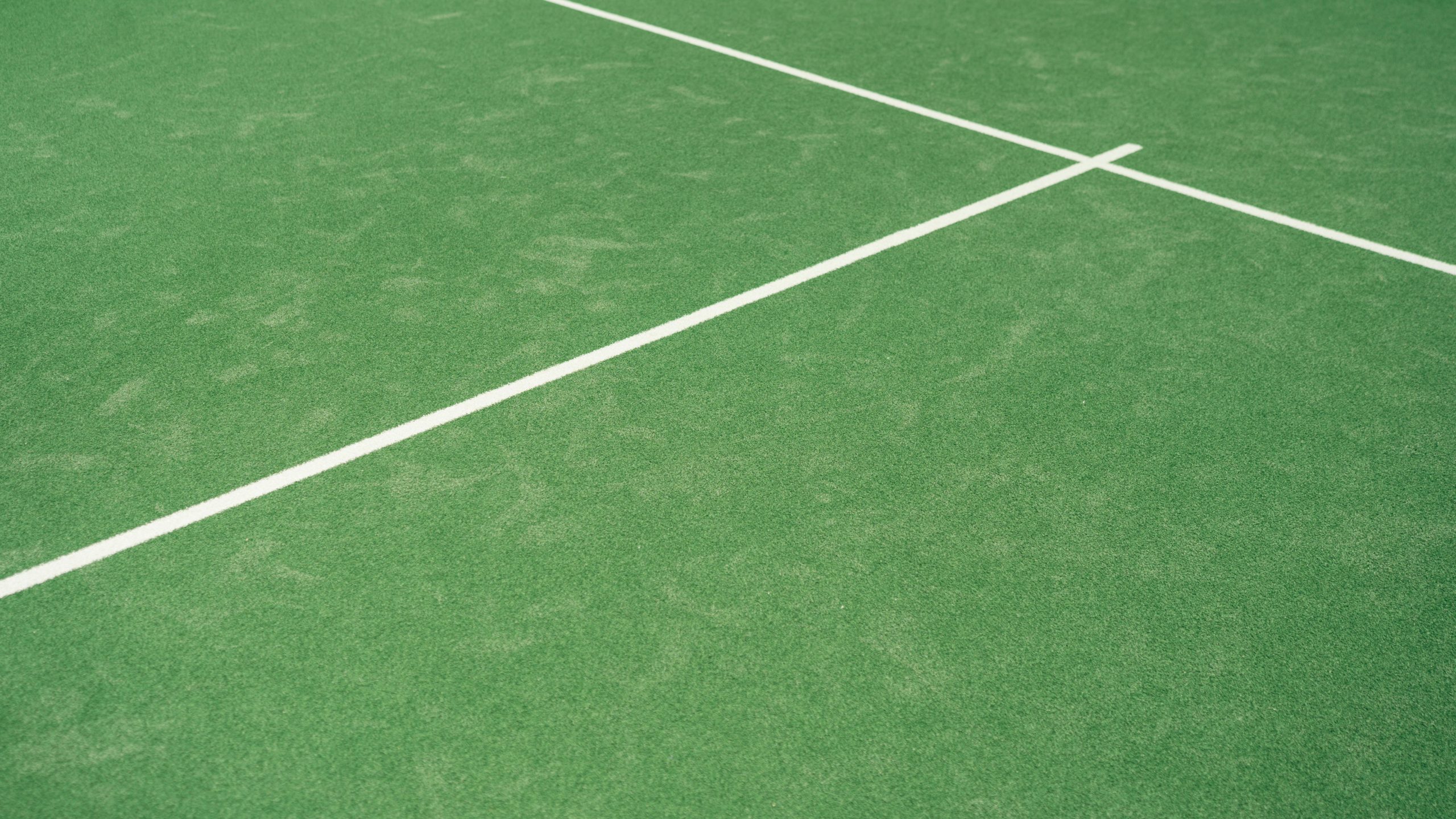 Close-up view of tennis court's vibrant green surface with white lines